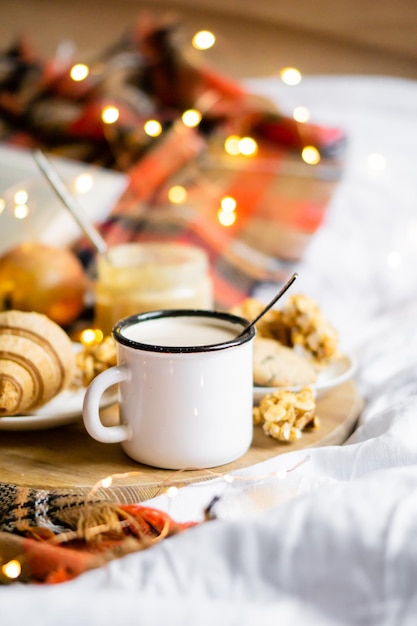 Semplice colazione casalinga di campagna a letto caffè con latte e pasticceria fatta in casa su coperta a quadri