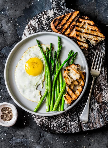 Semplice colazione rustica con asparagi all'uovo fritto e pane grigliato su sfondo scuro