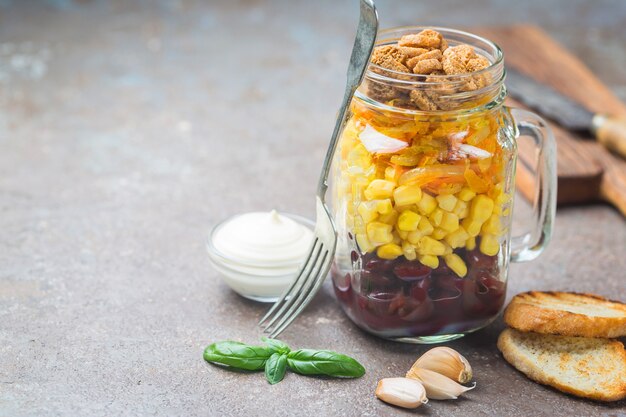 Semplice insalata casalinga in barattolo di vetro con mais, cipolla, fagioli, carote, crostini di pane e maionese