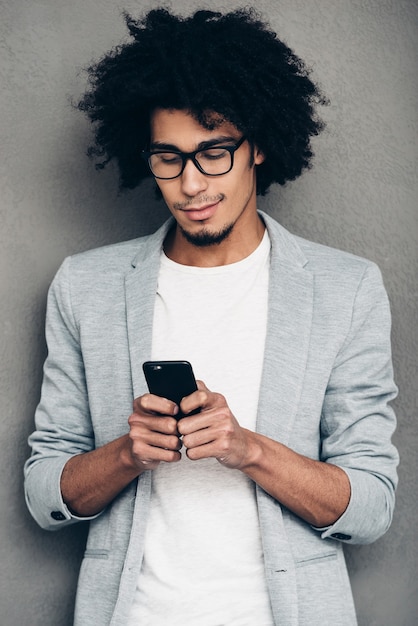 Sempre in contatto. Bel giovane africano che tiene lo smartphone e lo guarda stando in piedi