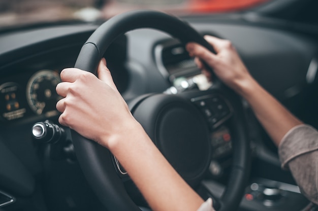 Sempre in movimento. Primo piano delle mani femminili sul volante durante la guida di un'auto