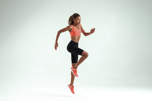 Sempre più alto. Vista laterale della giovane donna africana con un corpo perfetto in abbigliamento sportivo che salta durante l'allenamento in studio. concetto di sport. Motivazione. Uno stile di vita sano