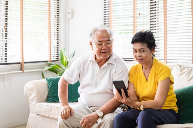 Senior Asian coupleGrey capelli utilizzando il telefono cellulare rilassarsi sul divano del soggiorno a casa anziani con il concetto di tecnologia