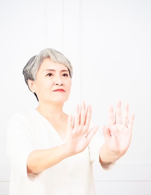 Senior bella donna dai capelli grigi che indossa un abito casual facendo segnale di stop con il palmo della mano. Espressione di avvertimento con gesto negativo e serio sul viso.