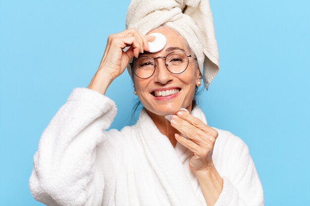 Senior bella donna pulizia del viso o trucco dopo la doccia indossando accappatoio