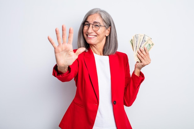 Senior bella donna sorridente e dall'aspetto amichevole, mostrando il numero cinque. concetto di affari e banconote