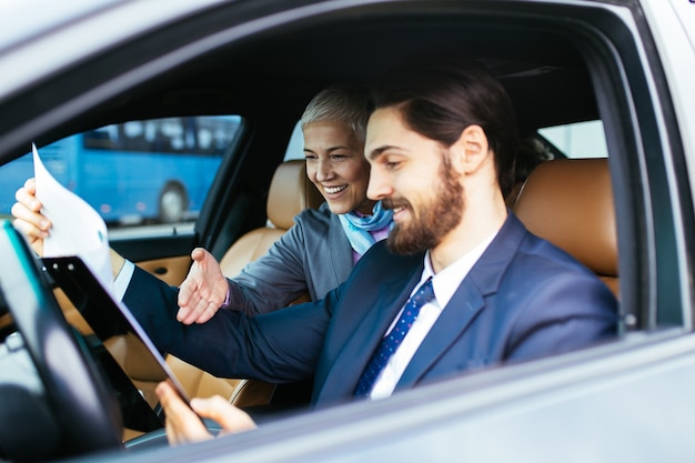 Senior business donna seduta in limousine e parlando con il suo autista. Concetto di affari.