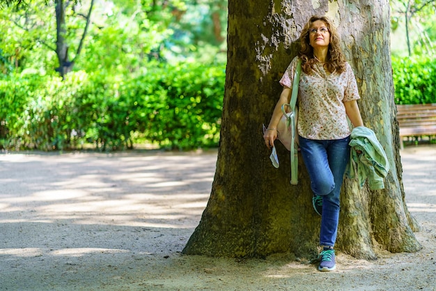 Senior donna appoggiata sul tronco di un enorme albero alla luce del caldo sole primaverile