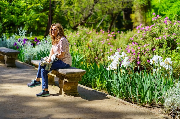 Senior donna bianca seduta su una panchina di pietra in un parco con molti fiori