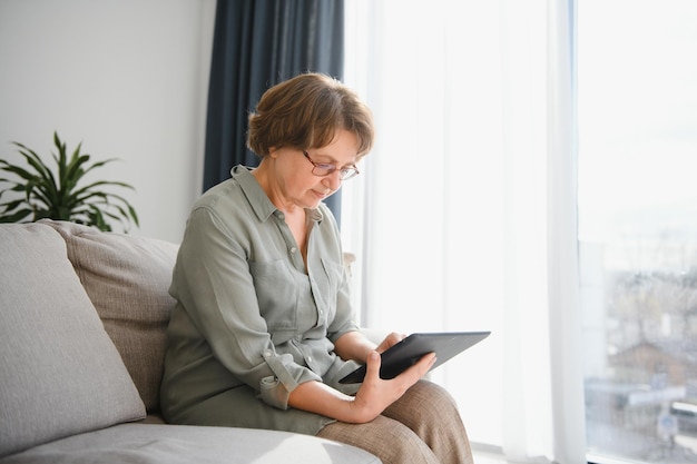 Senior donna che guarda e ride della sua tavoletta digitale sul divano