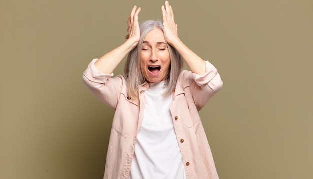 Senior donna che si sente stressata e ansiosa, depressa e frustrata con un mal di testa, alzando entrambe le mani alla testa