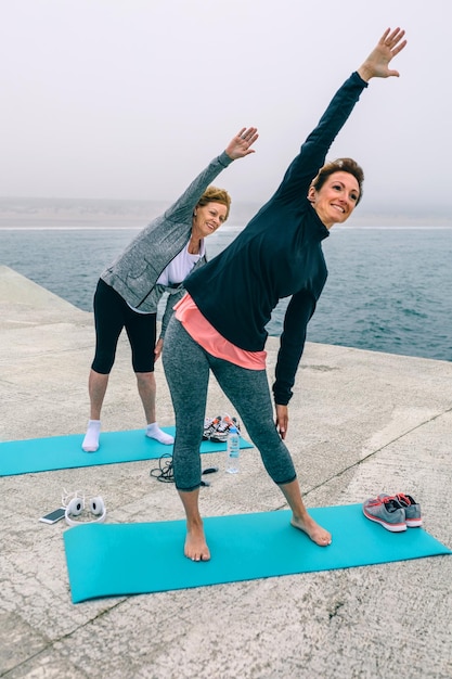 Senior donna con allenatore femminile che si estende a fianco del molo del mare