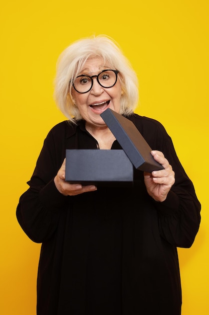 Senior donna con faccia sorpresa aprendo una scatola su sfondo giallo