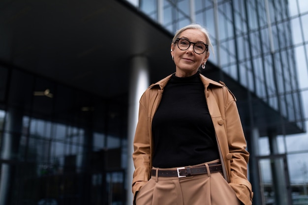 Senior donna d'affari sullo sfondo di un edificio per uffici guarda la telecamera con un sorriso