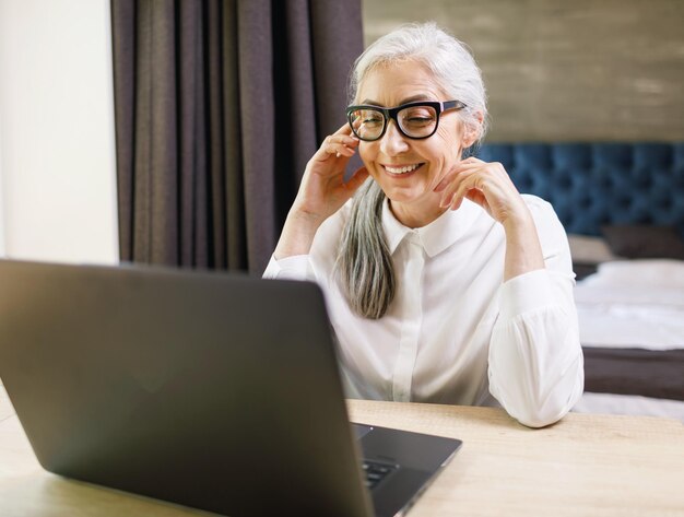 Senior donna dai capelli lunghi che indossa occhiali utilizzando la videochat e ha una conversazione piacevole