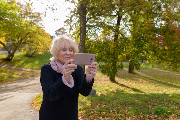 Senior donna felice sorridente mentre si scatta una foto con il telefono cellulare sul percorso del parco naturale tranquillo e rilassante