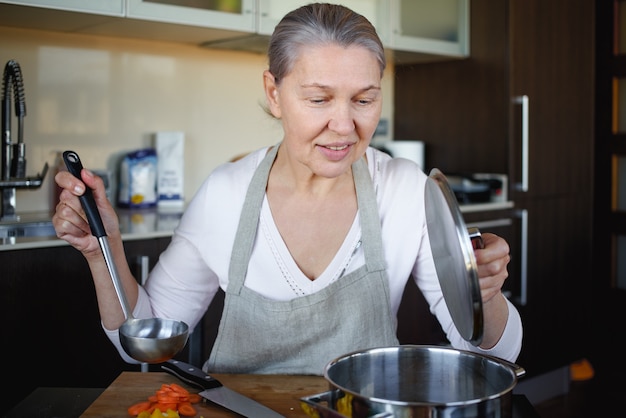 Senior donna in cucina per cucinare, mescolare il cibo in una pentola