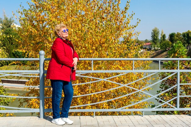 Senior donna in giacca rossa camminare e rilassarsi nella natura nel parco. Tempo autunnale