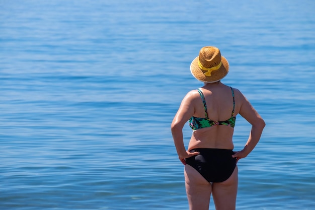 Senior donna in piedi da sola di fronte al mare mediterraneo su una spiaggia in una soleggiata giornata estiva