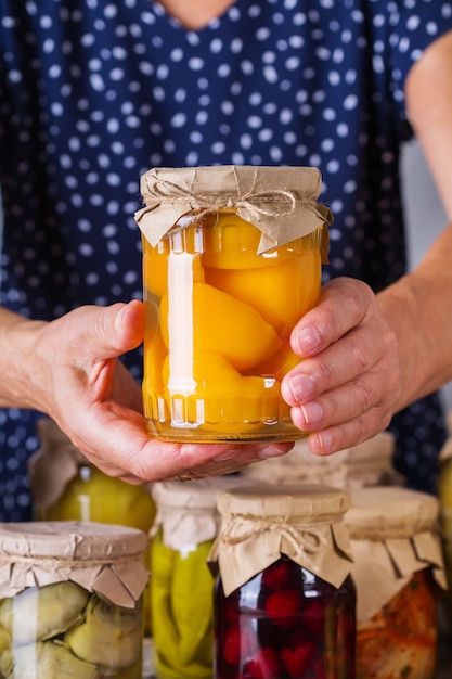 Senior donna matura che tiene in mano il barattolo con cibi conservati e fermentati fatti in casa. Varietà di verdure sott'aceto e marinate, composta di frutta. Pulizie, economia domestica, conservazione del raccolto