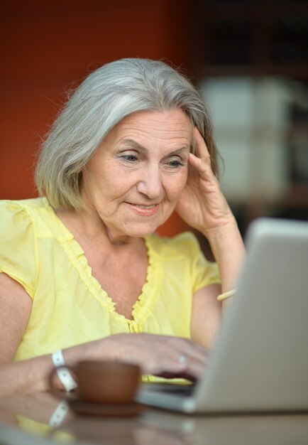 Senior donna seduta con laptop e caffè in hotel