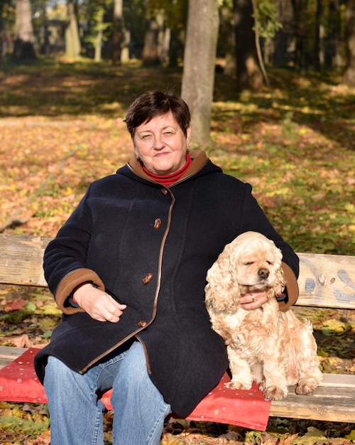 Senior donna seduta su una panchina con un cane nel parco autunnale