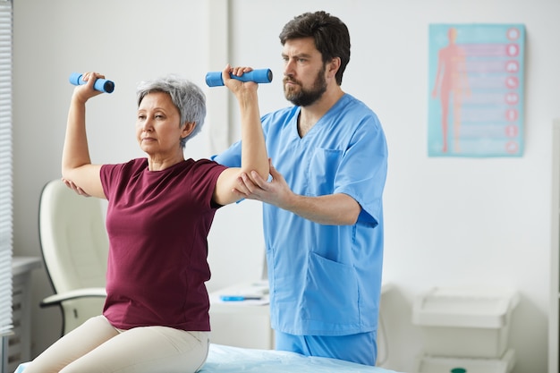 Senior donna sollevamento manubri e medico maschio che la assiste durante la riabilitazione