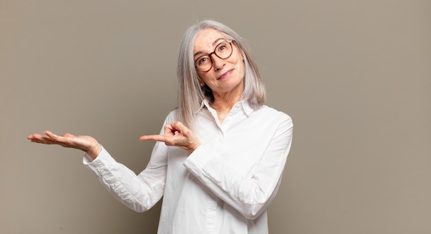 Senior donna sorridente allegramente e indicando lo spazio della copia sul palmo laterale, mostrando o pubblicizzando un oggetto