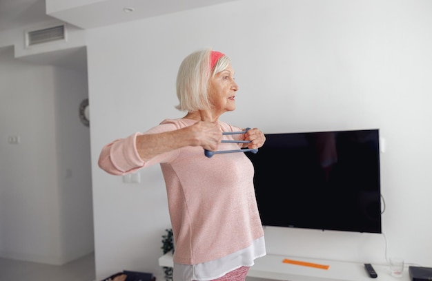 Senior donna stretching attrezzature per esercizi in camera accogliente