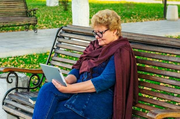 Senior donna utilizzando tablet leggendo e-book in un parco