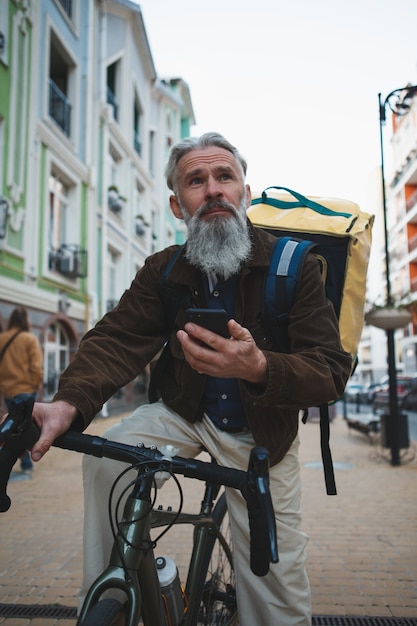 Senior fattorino riing bicicletta utilizzando smart phone