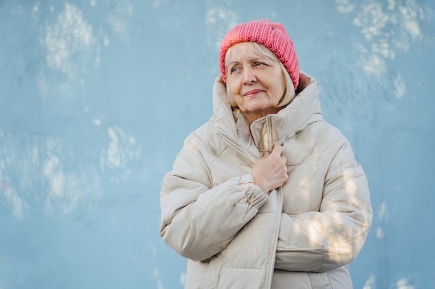 Senior femminile in capispalla alla moda. Donna anziana in cappello rosa lavorato a maglia sorridente