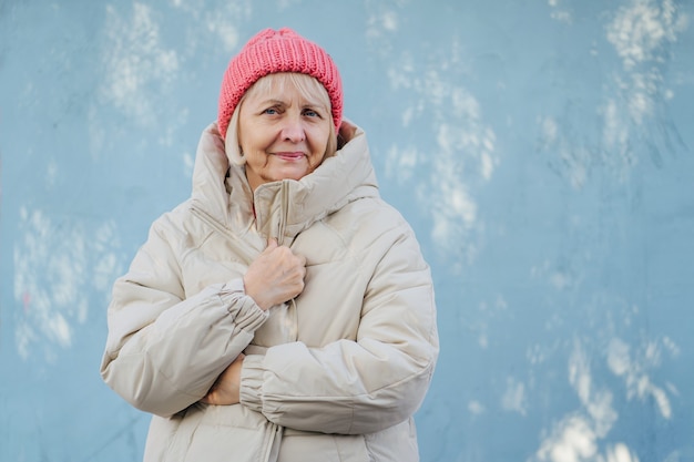 Senior femminile in capispalla alla moda. Donna anziana in cappello rosa lavorato a maglia sorridente