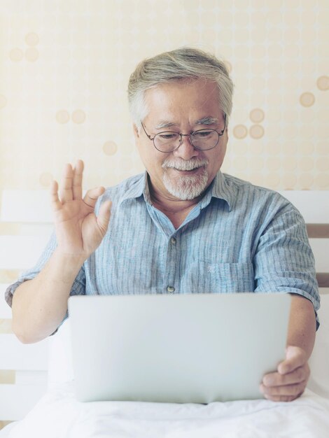 Senior maschio utilizzando un computer portatile faccia tempo chiamata a parenti discendenti parenti nipote sorridente sentirsi felice a letto a casa stile di vita concetto senior