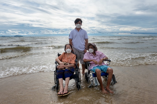 Senior persona disabile in sedia a rotelle in spiaggia contro lo sfondo del tramonto.