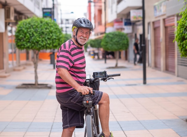 Senior sorridente ciclista uomo che indossa il casco in bicicletta la sua bicicletta elettrica in strada urbana smette di guardare indietro alla fotocamera nonno anziano attivo godendo di uno stile di vita sano e libertà