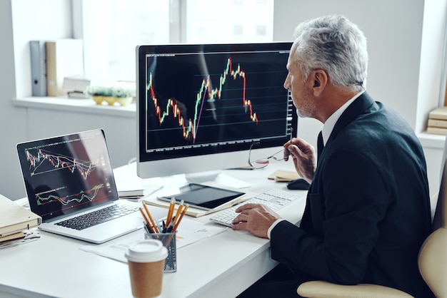 Senior trader in elegante tailleur che utilizza il computer mentre si lavora in ufficio