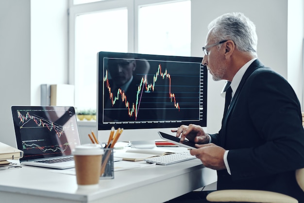 Senior trader in elegante tailleur che utilizza il computer mentre si lavora in ufficio