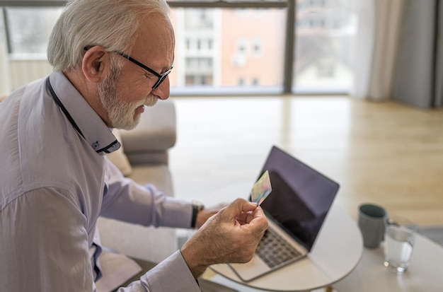 Senior uomo bello sorridente felice seduto a casa sua o in ufficio utilizzando il computer portatile