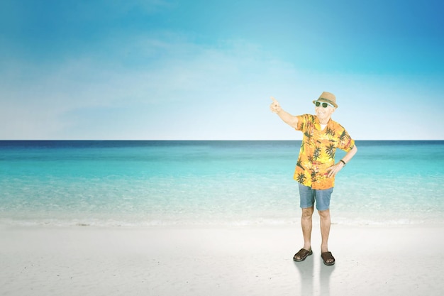 Senior uomo che punta a qualcosa sulla spiaggia tropicale