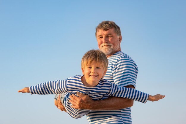 Senior uomo e bambino all'aperto sullo sfondo del cielo estivo. Nonno e ragazzo che si divertono insieme. Concetto di vacanza in famiglia. Buona festa del papà