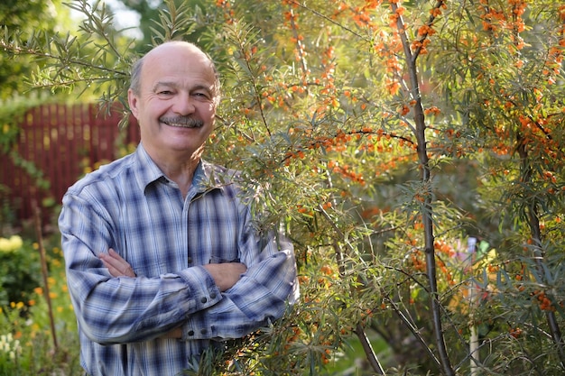 Senior uomo in piedi nel suo giardino vicino all'olivello spinoso sorridente