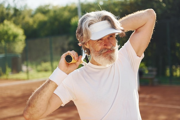 Senior uomo moderno ed elegante con racchetta all'aperto sul campo da tennis durante il giorno