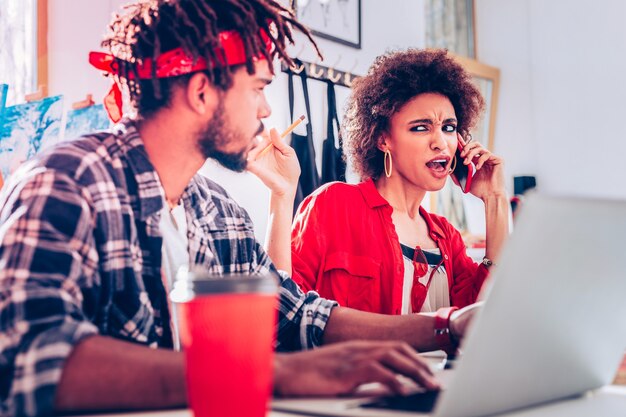 Sensazione eccessiva di emozioni. Ricci freelance donna dai capelli scuri che si sente ipermotivo mentre parla al telefono