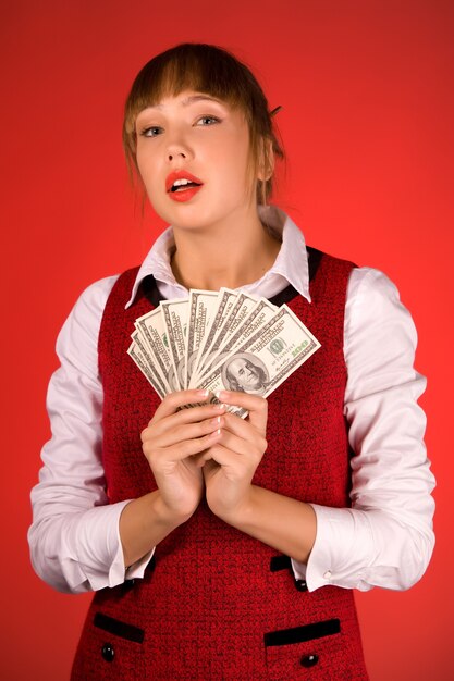 Sensuale giovane bella ragazza in abbigliamento casual sta tenendo un pacco di dollari sul rosso