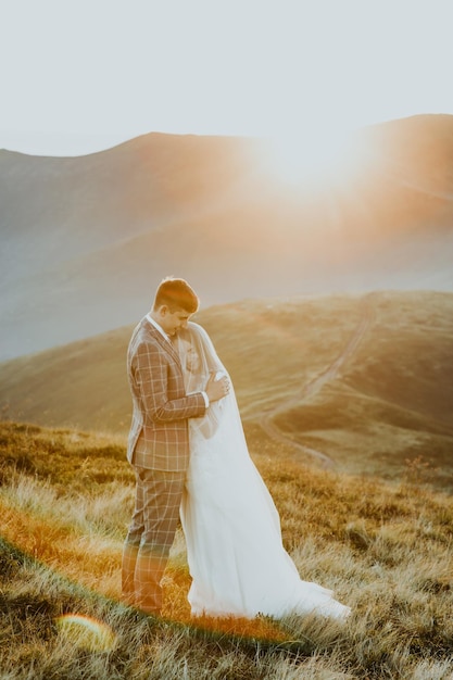 Sensuali sposi sposi e sposa in un lungo abito bianco in piedi sul bordo delle montagne