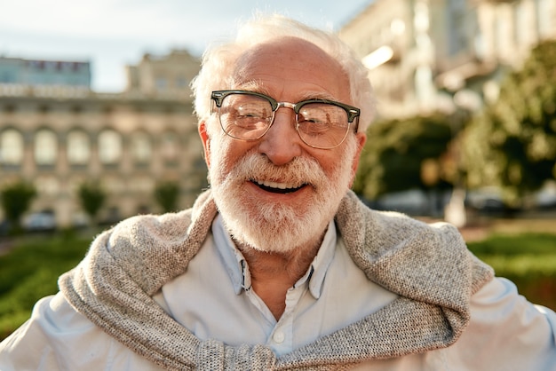 Sentendosi così felice ritratto di un bell'uomo anziano barbuto con gli occhiali che guarda la macchina fotografica e sorride