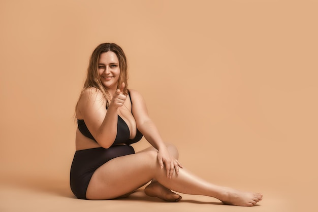 Sentendosi flirty bellissima modella sexy plus size in lingerie nera seduta sul pavimento e