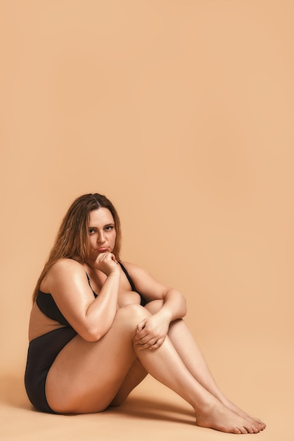 Sentendosi triste foto verticale del modello sexy plus size in lingerie nera seduto sul