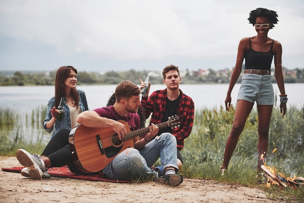 Senti la musica. Un gruppo di persone fa un picnic sulla spiaggia. Gli amici si divertono durante il fine settimana.